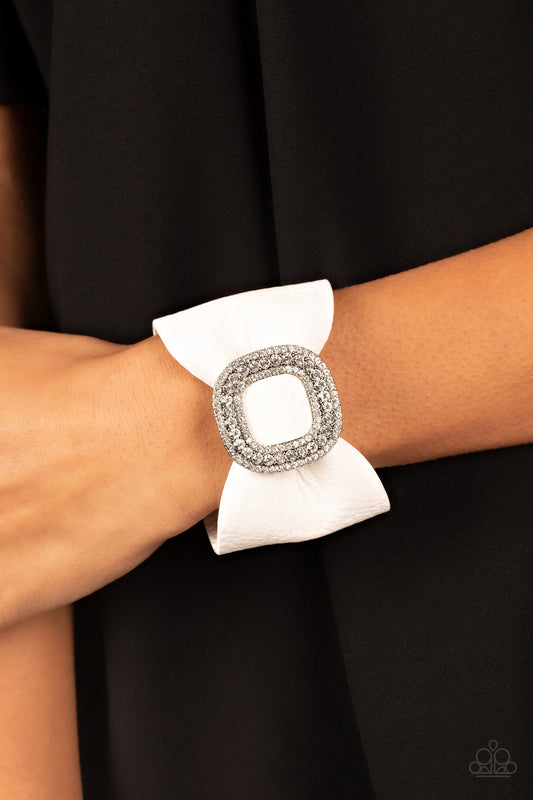 Paparazzi Lights, SELFIE, Action - White Leatherette Bracelets athick white pleather band delicately knots around the wrist. Stacked with brilliant white rhinestones, a dramatic silver buckle sparkles at the center of the wrist for a dramatic finish. Features an adjustable snap closure.  Sold as one individual bracelet.