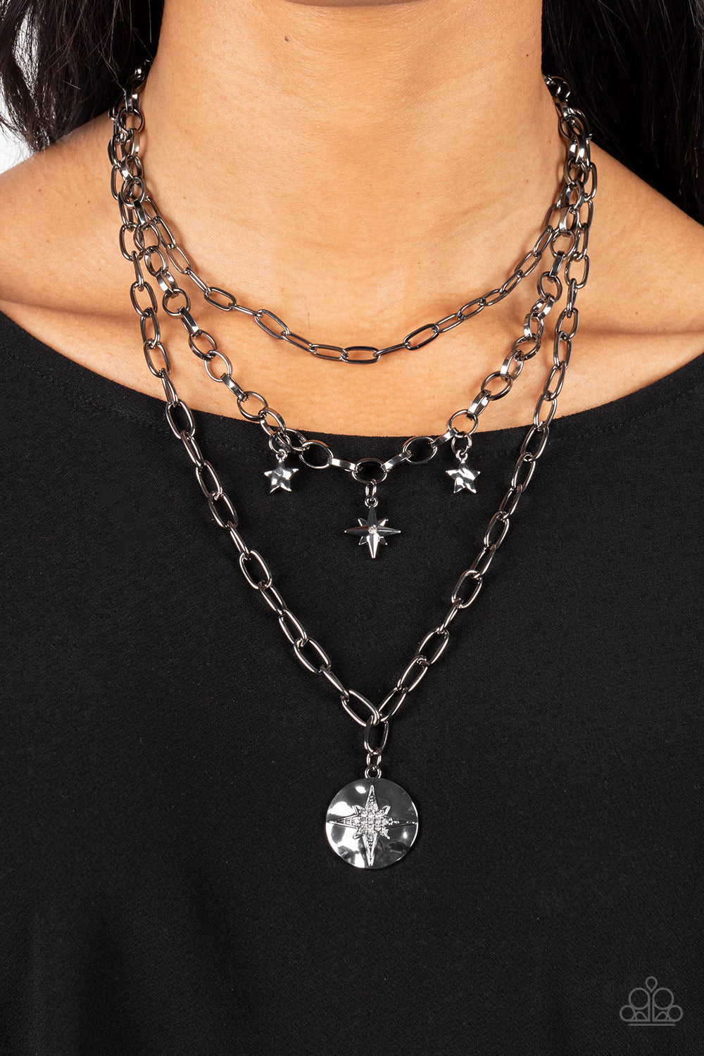 Paparazzi Under the Northern Lights - Black Star Necklaces three gritty gunmetal chains layer down the chest. Flanked by a pair of hammered gunmetal stars, a white rhinestone dotted star swings from the centermost chain above a hammered gunmetal frame twinkling with a white rhinestone dotted star design for a stellar finish. Features an adjustable clasp closure. Sold as one individual necklace. Includes one pair of matching earrings.