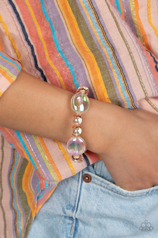 Bubbly iridescent beads in varying sizes are threaded along a stretchy band, creating a glittery magical effect around the wrist. Shiny copper cap fittings encase the smaller beads, adding vintage metallic detail to the effervescent design. Due to its prismatic palette, color may vary.  Sold as one individual bracelet.  Get The Complete Look! Necklace: "Prismatic Magic - Copper" (Sold Separately)