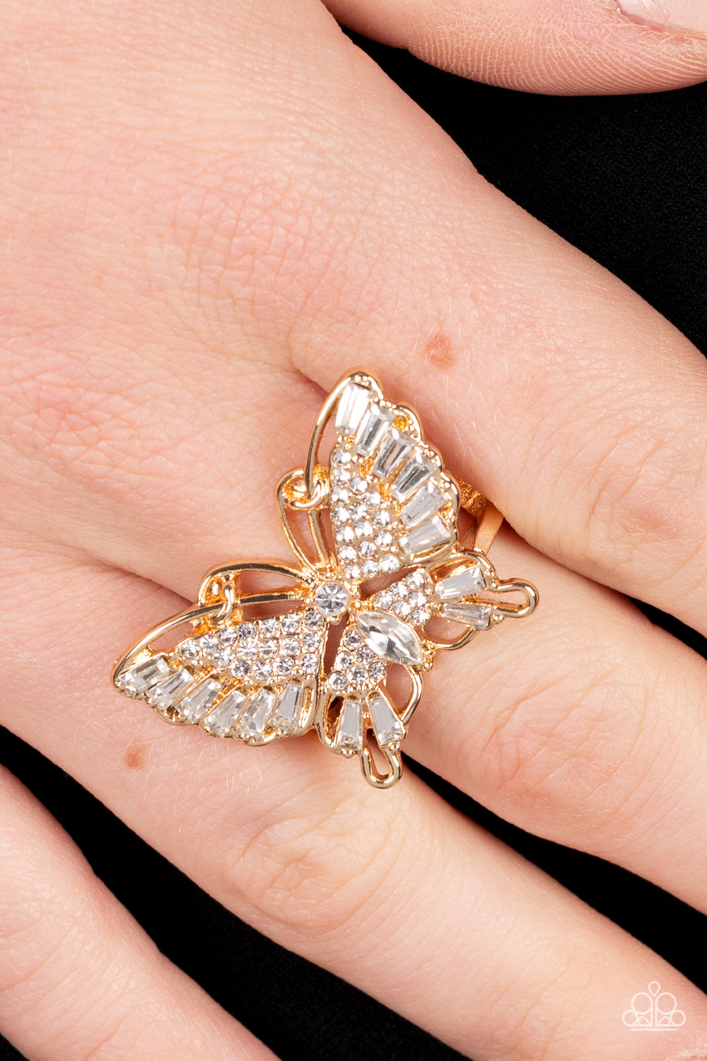 Paparazzi Accessories Fearless Flutter - Gold Butterfly Rings sparkling with round, teardrop, and emerald cut white rhinestones, a gold butterfly fearlessly flutters atop the finger for a statement-making finish. Features a stretchy band for a flexible fit.  Sold as one individual ring.