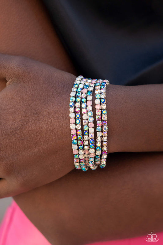 Embellished in rhinestone studs, six bracelets threaded along elastic stretchy bands stack across the wrist. Opalescent white, clear, and shades of iridescent in fuchsia, baby pink, and blues create a dramatic collision of color and shimmer. Due to its prismatic palette, color may vary.  Sold as set of six bracelets.