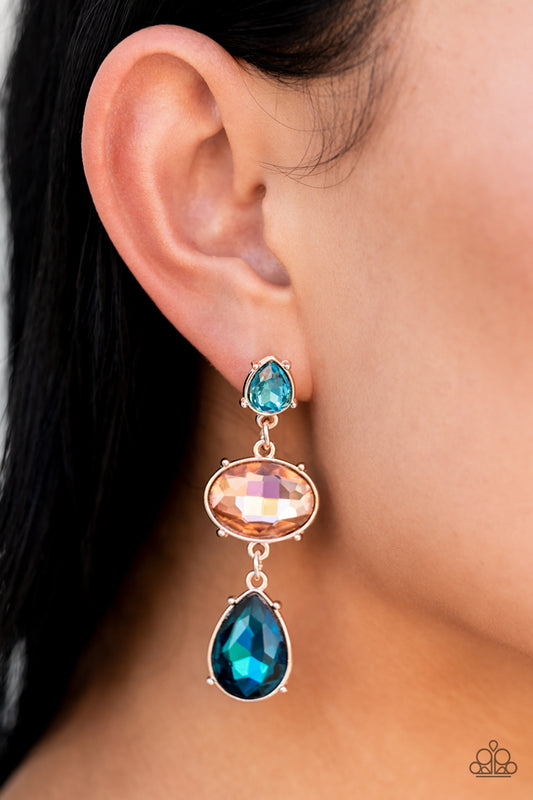 Paparazzi Accessories - Royal Appeal Multi Earrings - September 2022 LOP a small, light blue, teardrop-shaped gem gives way to a peachy oval-shaped rhinestone tilted on its side. A large, deep blue teardrop swings from the oval above, adding dramatic movement to the colorful display. Each faceted gem is set in pronged rose gold fittings, exaggerating their sparkle as they swing from the ear in a lustrous finish.  Sold as one pair of post earrings.