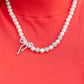 strand of classic white pearls coalesces down the neckline in a feminine display. Airy silver spheres, adorned in sparkling white rhinestones, are effortlessly sprinkled among the sea of pearls on one side, infusing the design with capricious shimmer. Then in the perfect finishing touch, a ribbon of silver, adorned in tiny white pearls and sparkling white rhinestones, loops into a bow at the bottom of the design. Features an adjustable clasp closure.