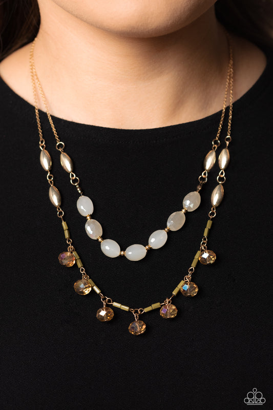 Two strands of dainty gold chain are adorned in a collection of white opaque beads, faceted glass beads, and gold accents, culminating in a layered design rich with vintage character. The glassy beads that swing along the lower chain feature a subtle reflective surface in a cozy peach glow, complementing the opaque beading that lines the chain above, with tiny gold and olive green accents sprinkled throughout the piece in a rustic finish. Features an adjustable clasp closure. 