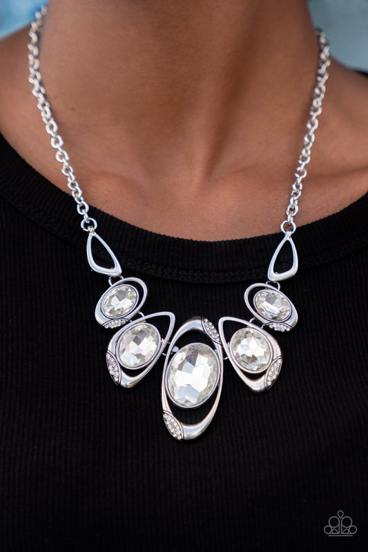 Paparazzi Hypnotic Twinkle - White April 2022 Life of the Party Necklaces dusted in sections of glassy white rhinestones, asymmetrical silver frames curl around oversized white gems below the collar. Varying in shape, the mismatched frames increase in size as they near the center for a hypnotizing finish. Features an adjustable clasp closure.  Sold as one individual necklace. Includes one pair of matching earrings.  Life of the Party exclusive item April 2022.  