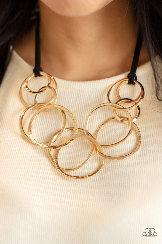 Paparazzi Accessories Spiraling Out of COUTURE - Gold Necklaces black suede cords knot around a mismatched assortment of hammered gold rings that interlock below the collar, creating two rows of dizzying texture. Features an adjustable clasp closure. Sold as one individual necklace. Includes one pair of matching earrings.