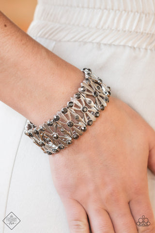 Paparazzi Thematic Twinkle - Silver Bracelets dotted with layers of smoky hematite rhinestones, flared and textured silver bars crisscross and merge into shiny silver frames. Threaded along stretchy bands, the smoldering frames create an intensely swanky fashion around the wrist.  Sold as one individual bracelet.  Magnificent Musings Fashion Fix February 2022